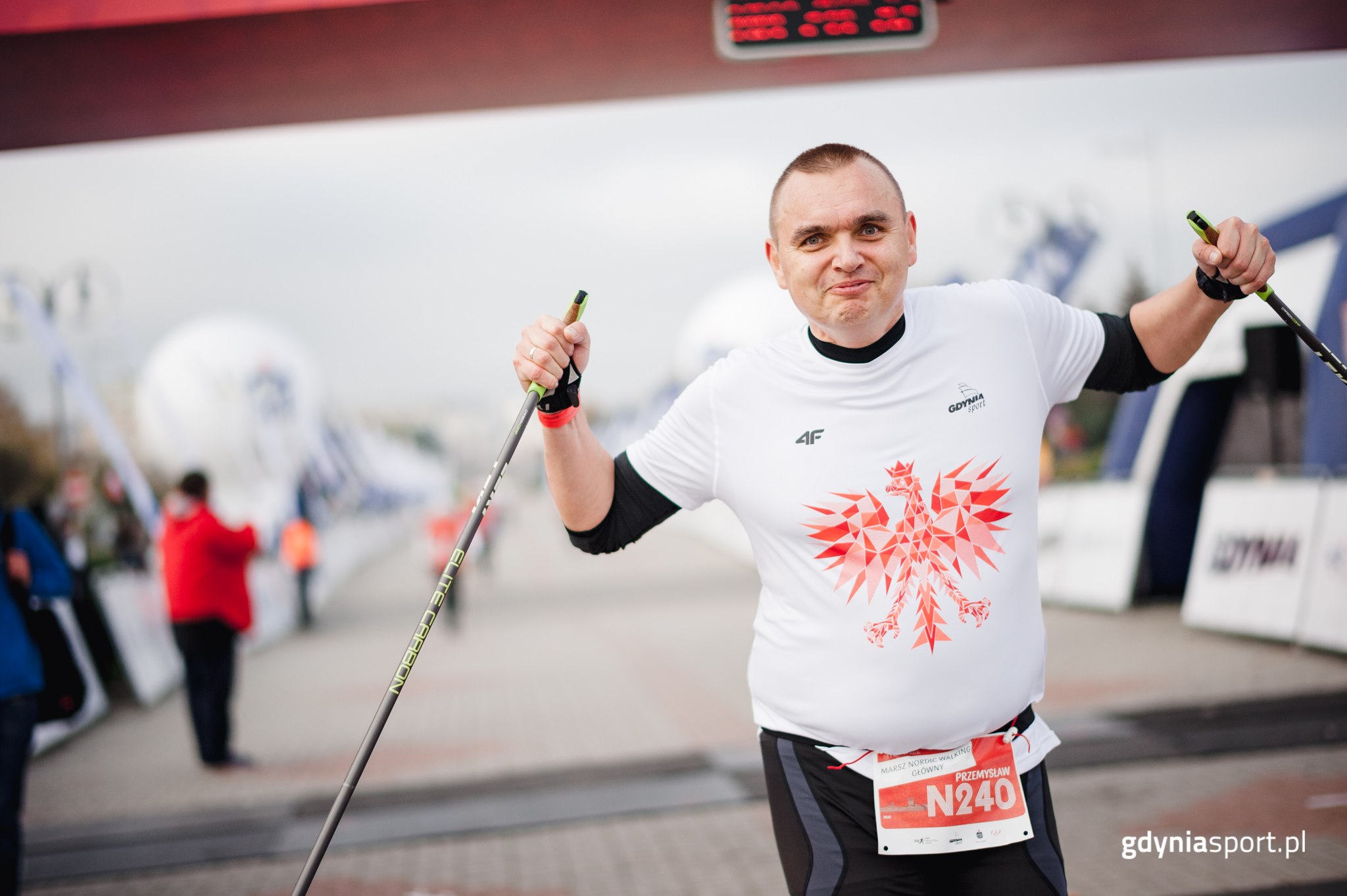 Przemysław Dalecki na mecie marszu niepodległości w koszulce z orłem i podniesionymi w górę kijami od nordic walking